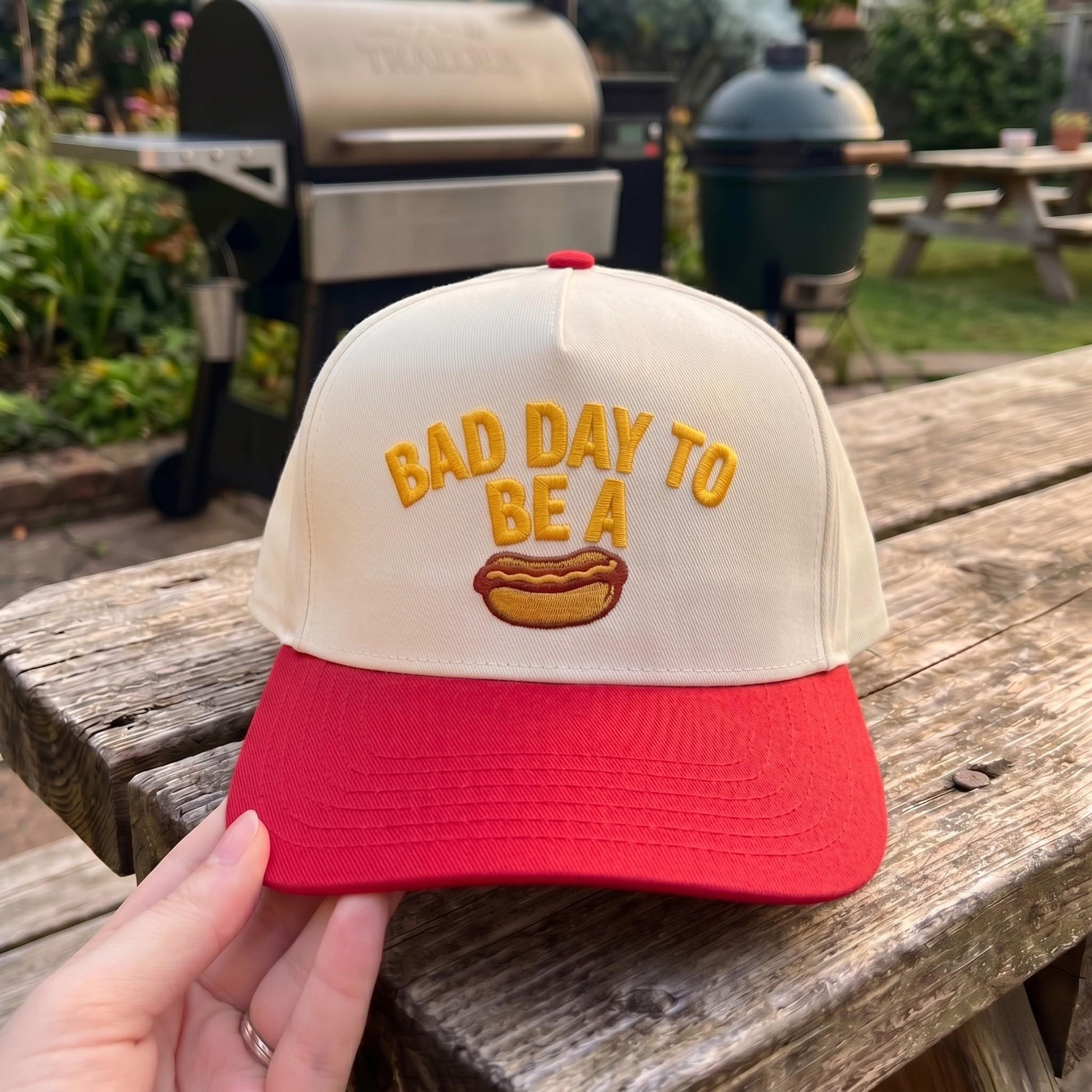 Embroidered snapback hat with 'Bad Day to Be a Hotdog' design in red and cream, displayed outdoors