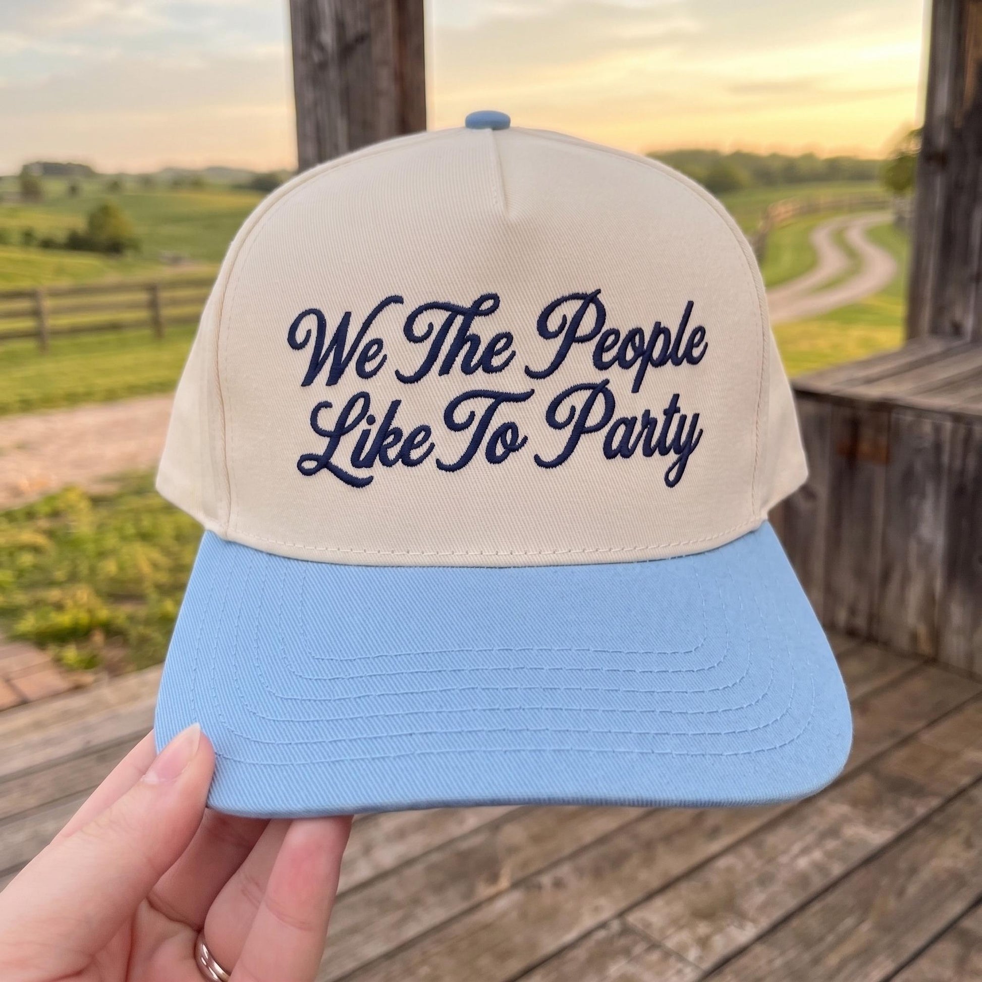 Embroidered baseball cap with 'We The People Like To Party' design in a rural setting