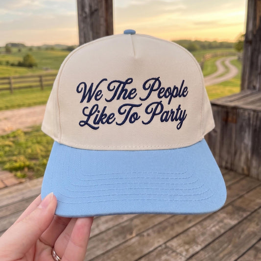 Embroidered baseball cap with 'We The People Like To Party' design in a rural setting