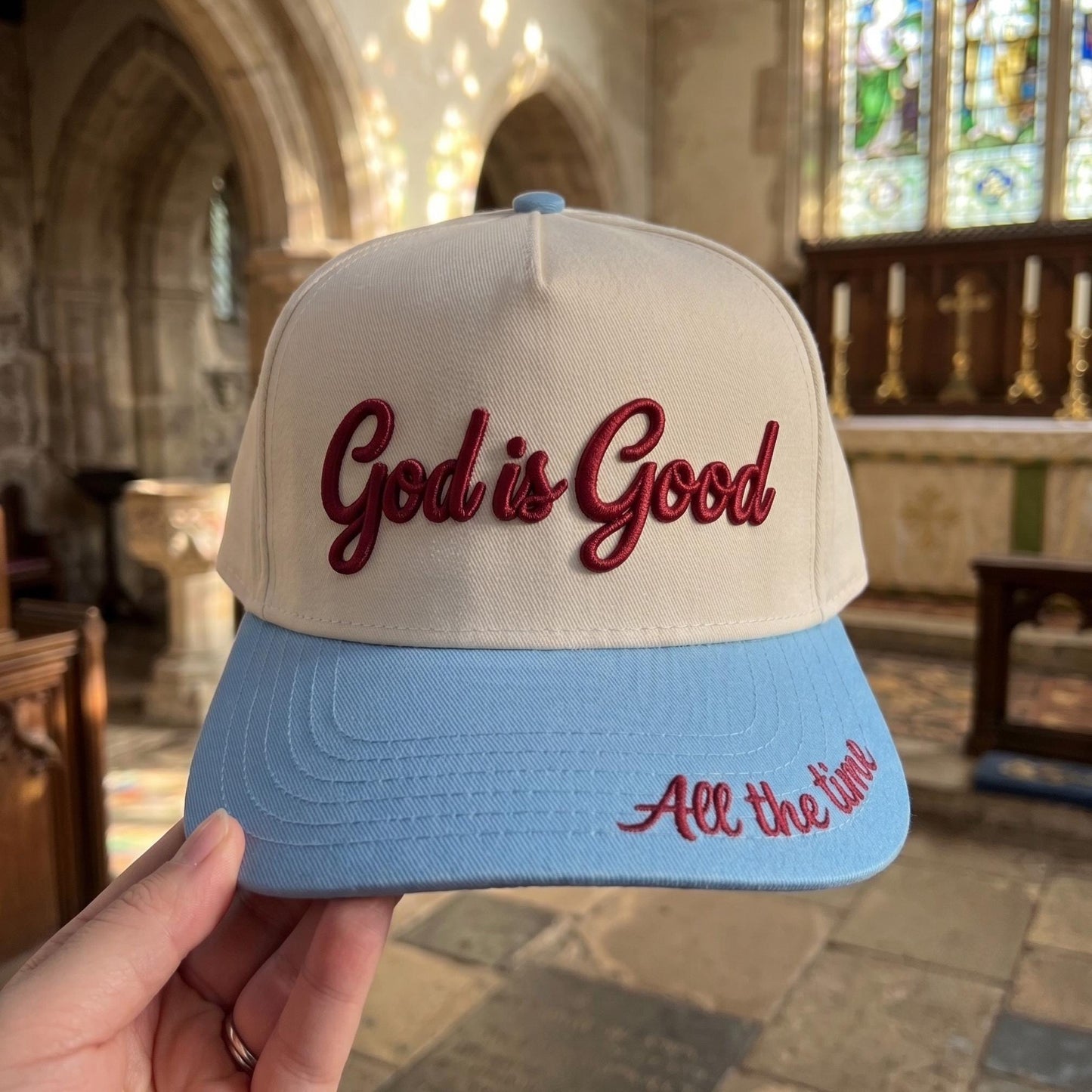 God is Good' embroidered baseball cap with beige crown and blue bill in church setting