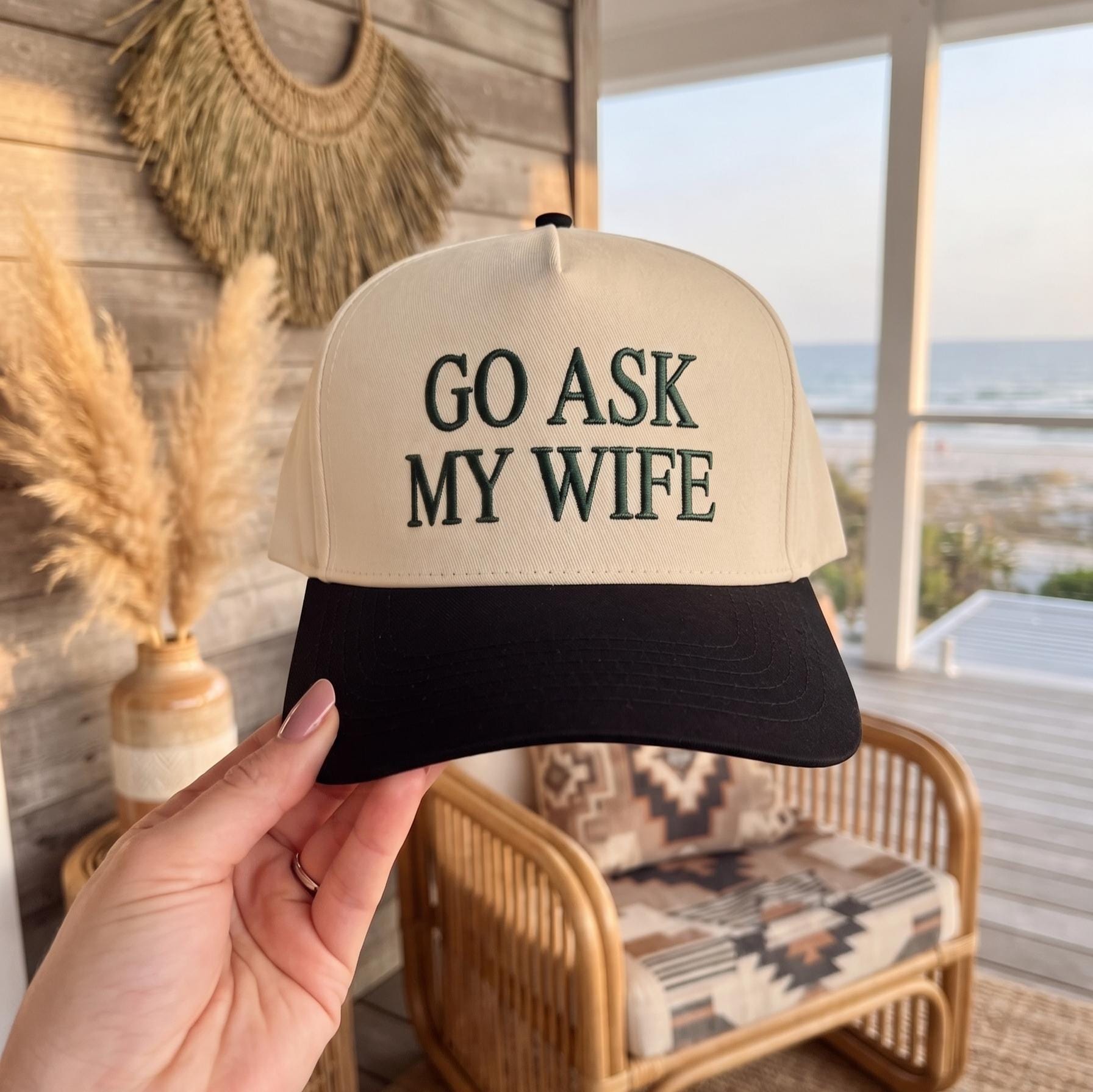 Embroidered baseball cap with 'Go Ask My Wife' text in beige and black displayed in a sunny outdoor setting