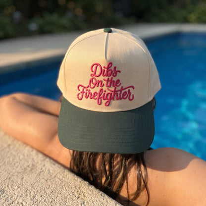 Novelty baseball cap with 'Dibs On the Firefighter' embroidery in beige and green by a swimming pool