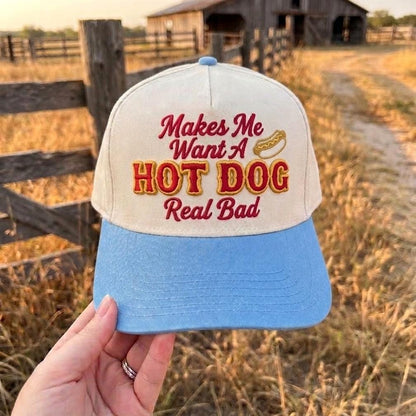 Funny embroidered hot dog cap in white and blue with playful message held in rustic outdoor setting