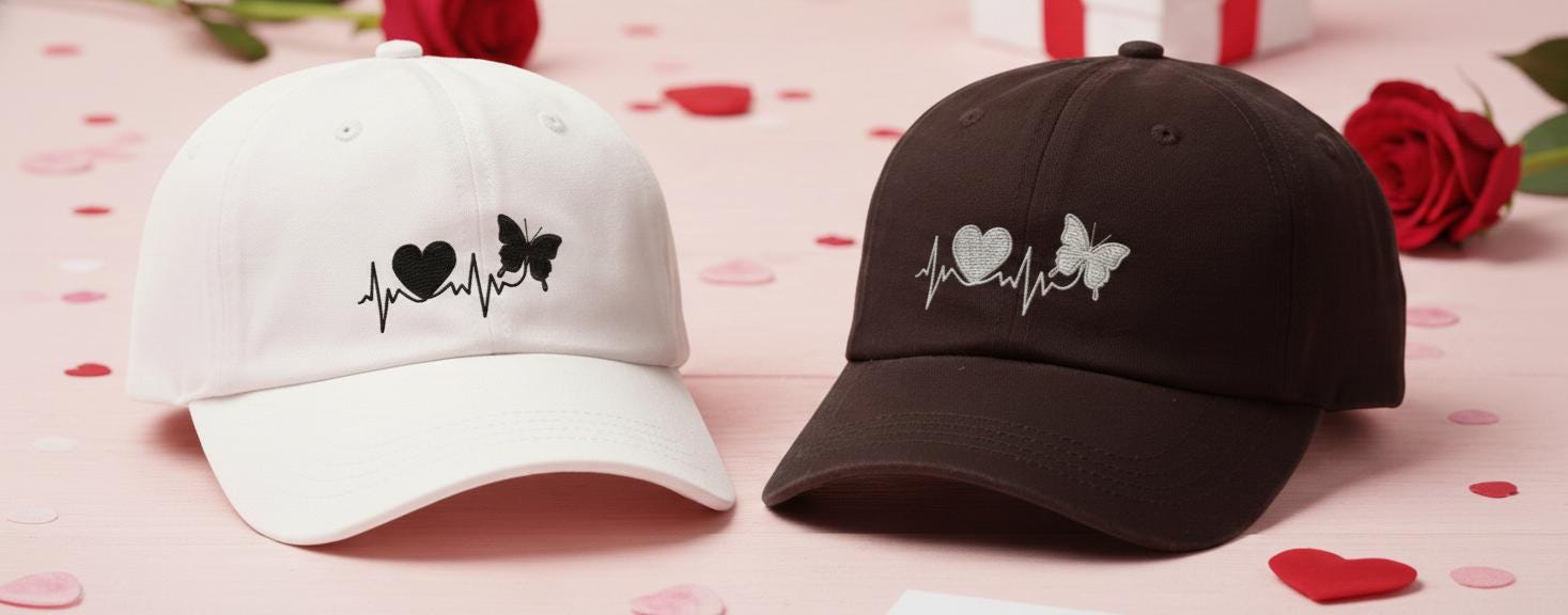White and black baseball caps with embroidered heartbeat design featuring a heart and butterfly, set on a romantic