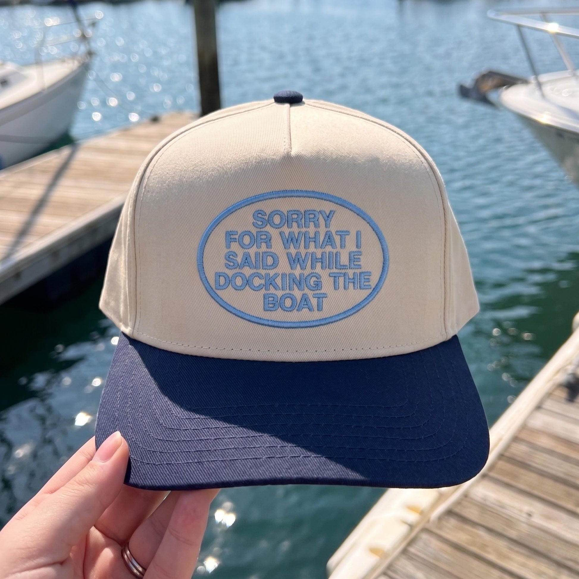 Navy and beige cap with humorous embroidery 'Sorry for What I Said While Docking the Boat' on dock setting