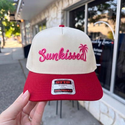 Custom tan and red 'Sunkissed' cap with pink embroidery and palm tree logo in urban setting