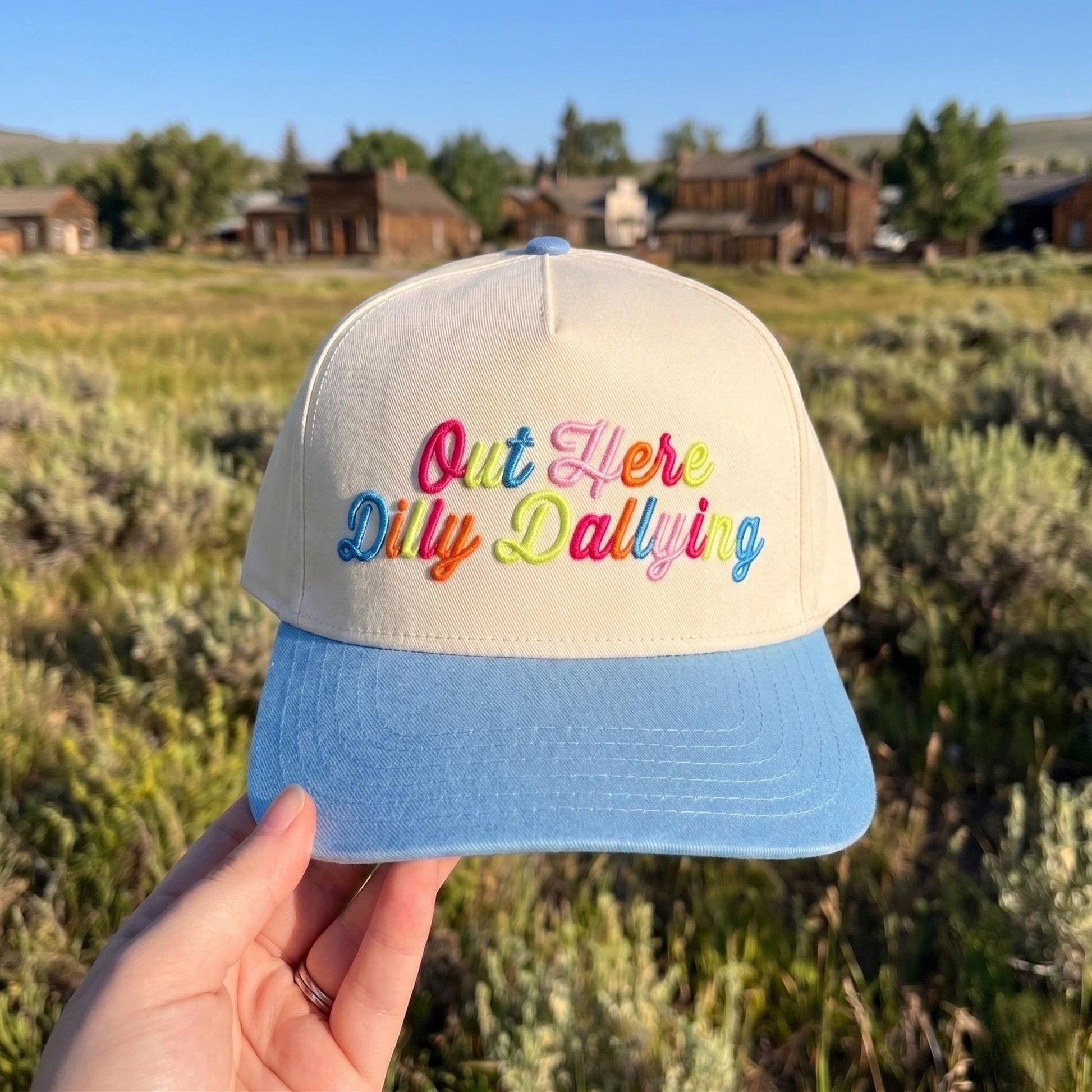 Colorful embroidered baseball cap with 'Out Here Dilly Dallying' design, off-white base, blue brim