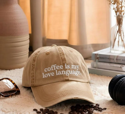 Tan baseball cap with 'coffee is my love language' quote displayed in a cozy setting