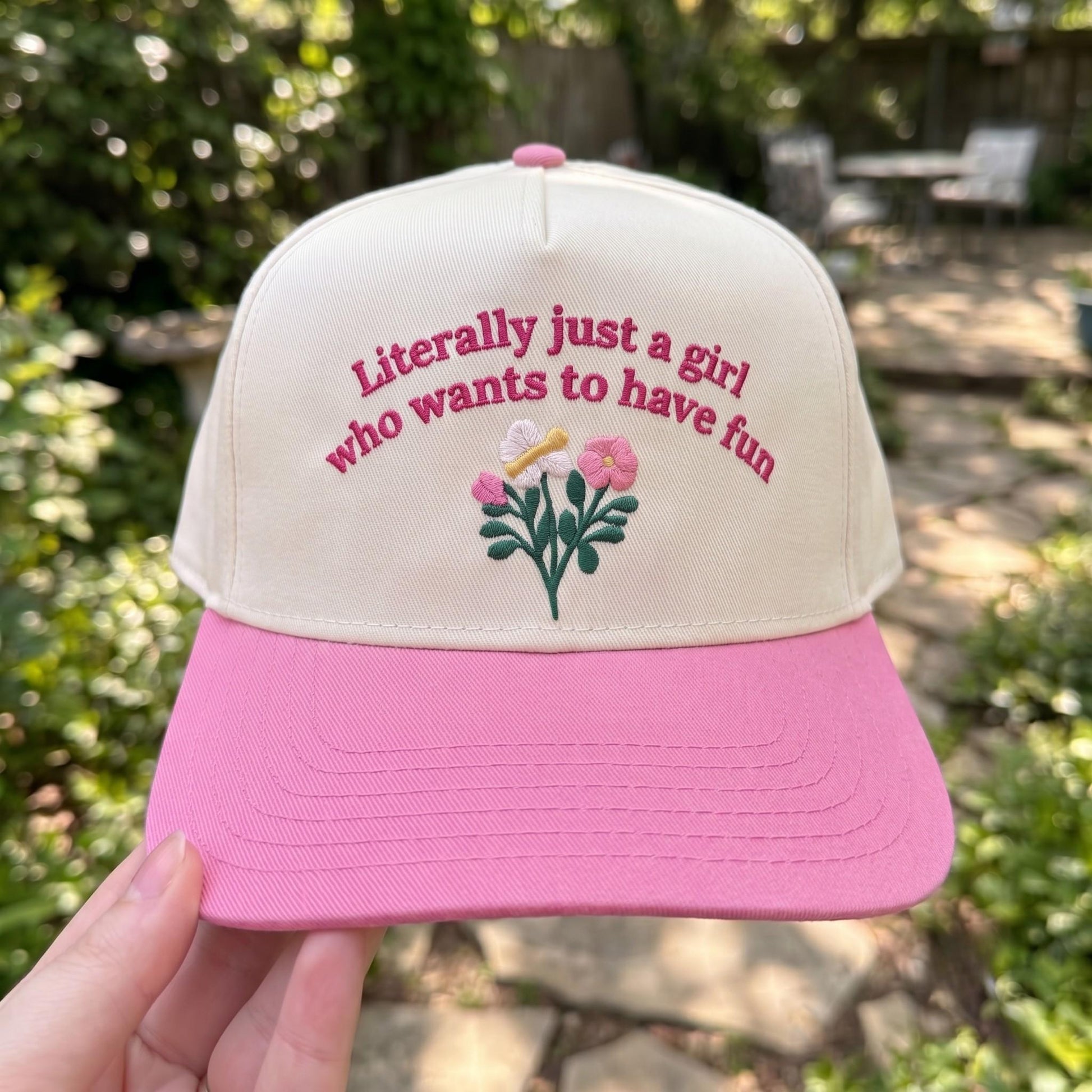 Trendy floral embroidered cap with pink brim and fun text in a garden setting