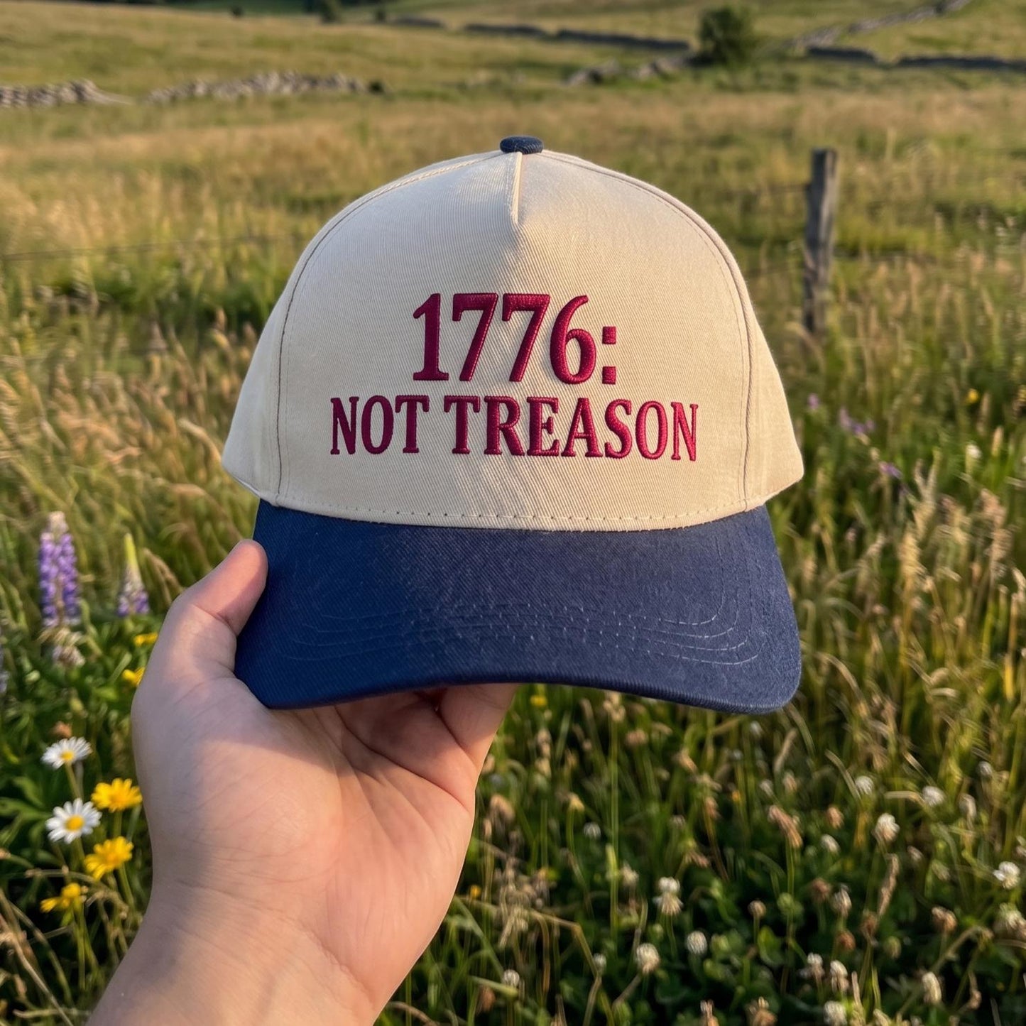 1776: Not Treason' embroidered trucker hat with beige front and navy brim in a field setting