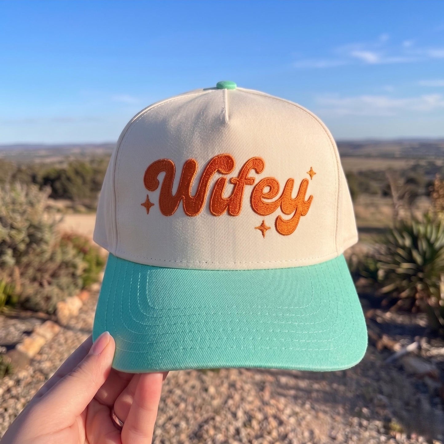 Trendy Wifey cap with cream crown and teal brim against an outdoor backdrop