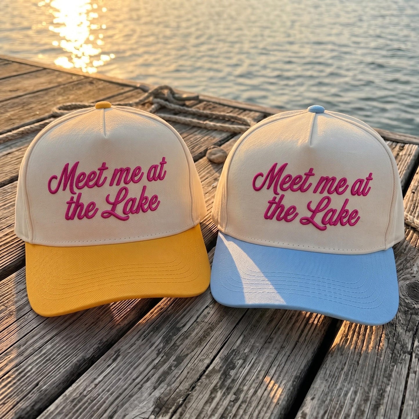 Trendy caps with 'Meet me at the Lake' embroidery, yellow and blue brims on wooden dock by lake