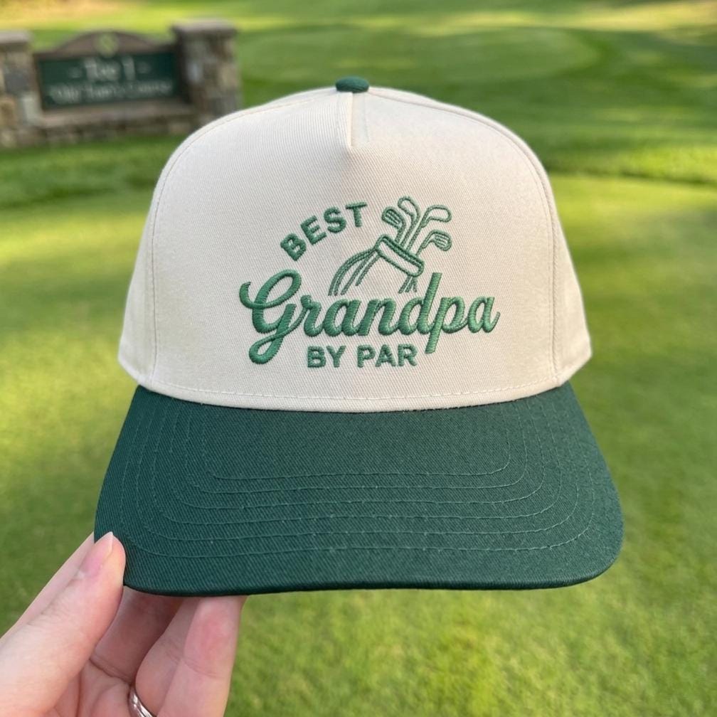 Best Grandpa by Par golf hat with embroidered text and green brim displayed on a golf course