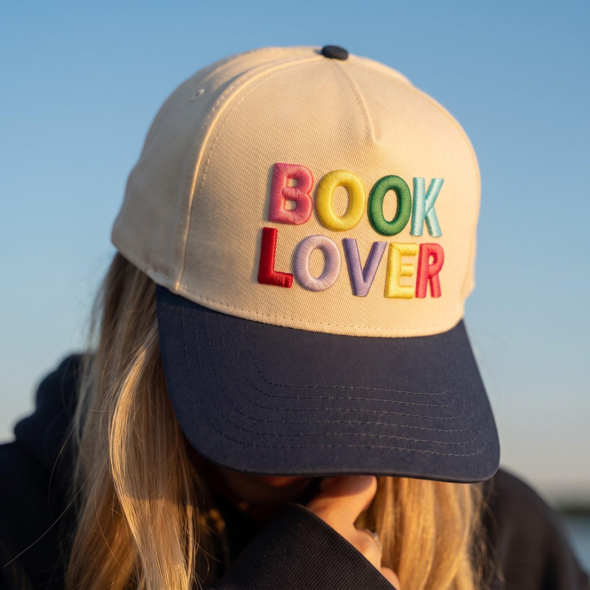 Book Lover' embroidered baseball cap in cream and navy with colorful letters in outdoor setting