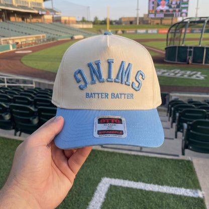 Retro baseball cap featuring a reversed text design in blue and cream colors at a baseball field