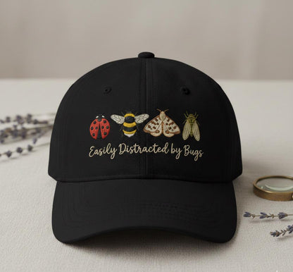 Black baseball cap with embroidered insect designs and 'Easily Distracted by Bugs' slogan
