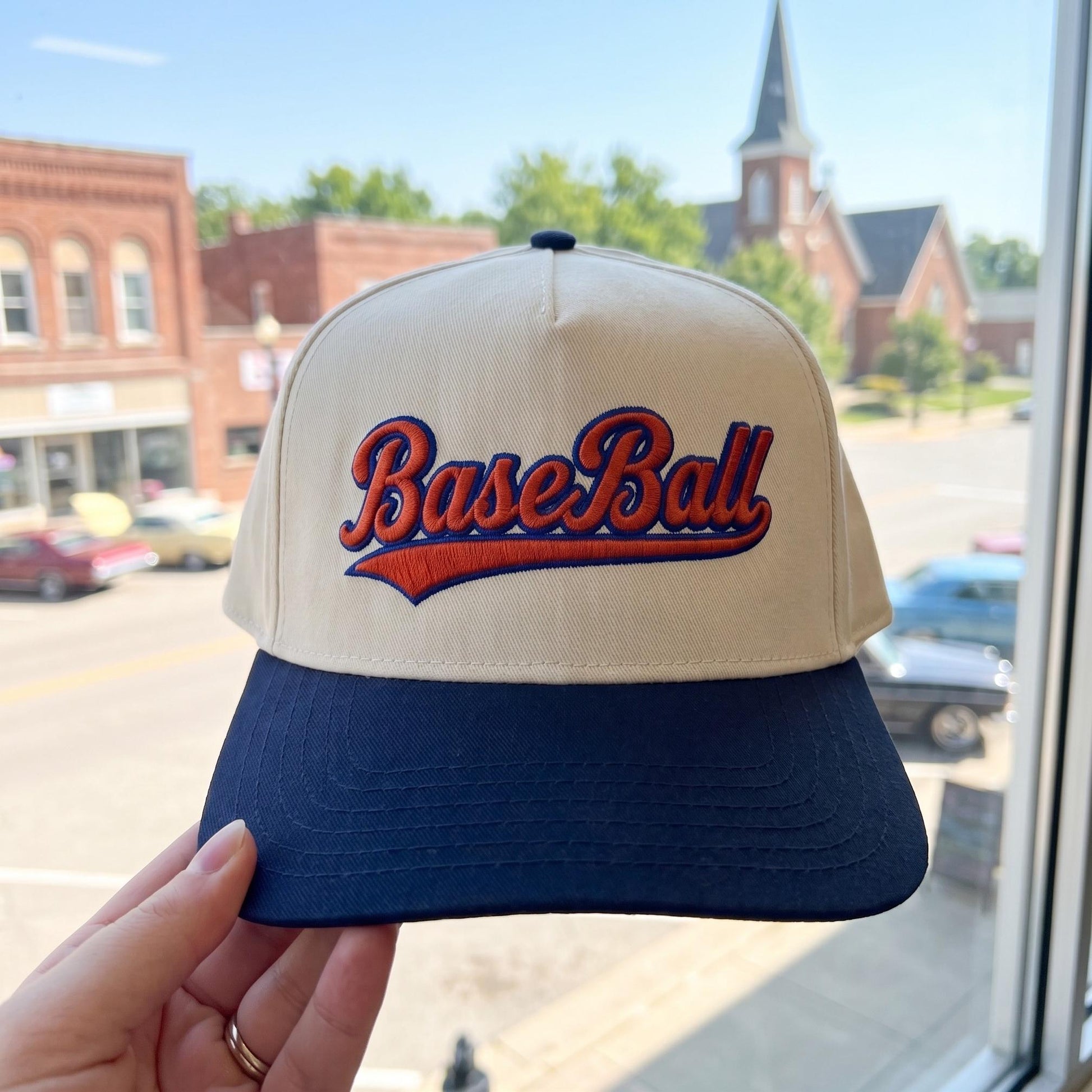 Vintage style baseball cap with embroidered 'Baseball' lettering in cream and navy on a street background