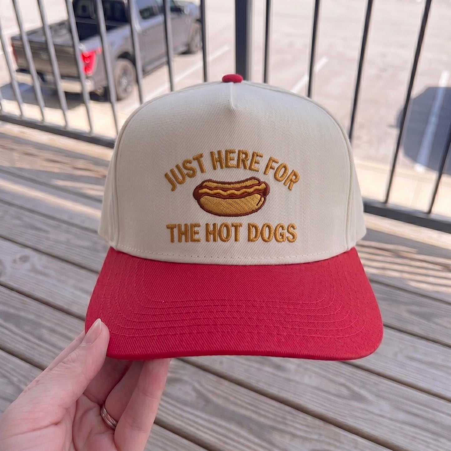 Retro baseball cap with hot dog embroidery, cream front with red brim, wooden background