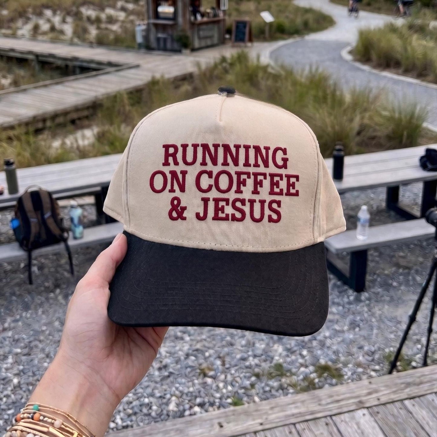 Unique baseball cap with 'Running on Coffee & Jesus' slogan, beige and black design, outdoors setting