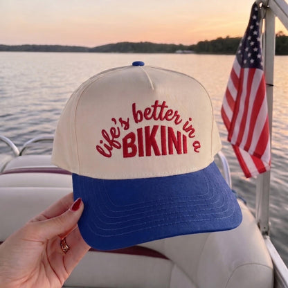 Stylish two-tone cap with royal blue brim and bold red 'Bikini' slogan held on a boat