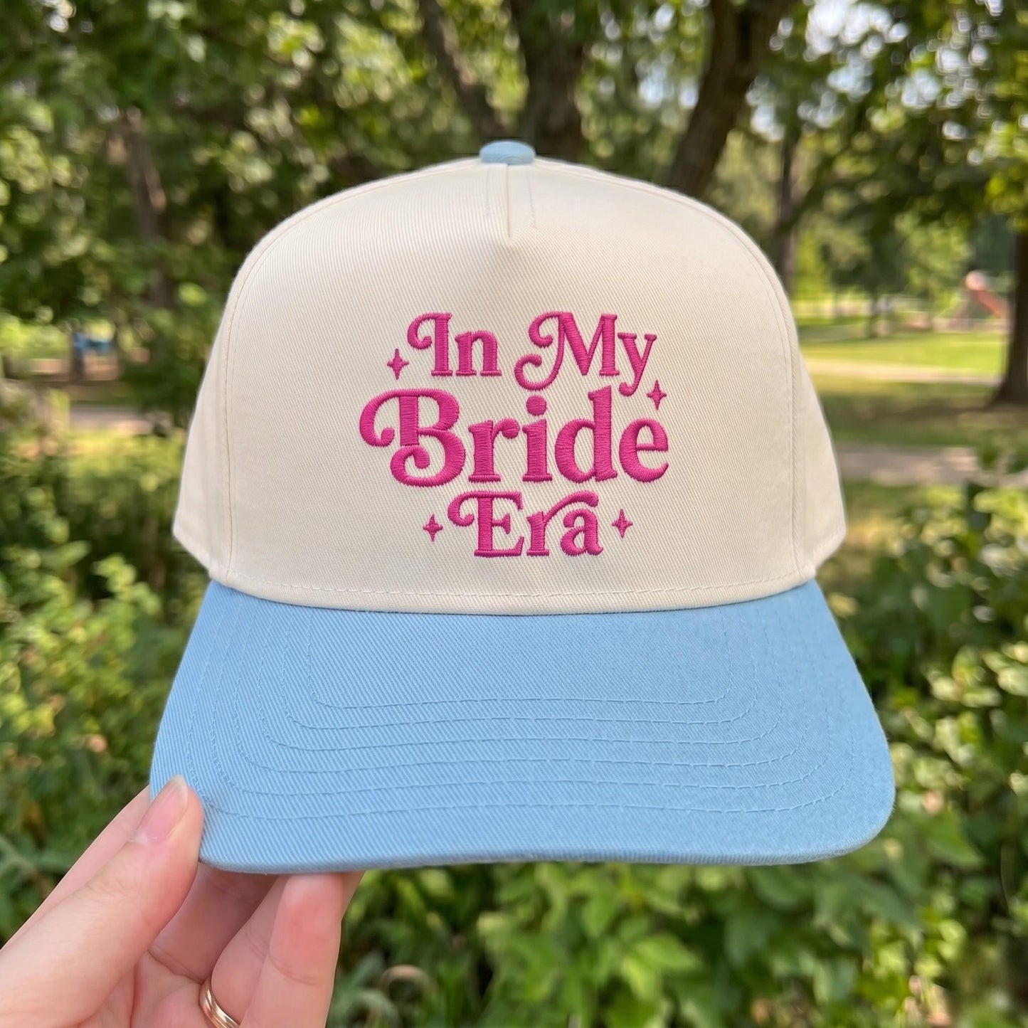 In My Bride Era' embroidered cap with ivory crown and blue visor, displayed in a park setting